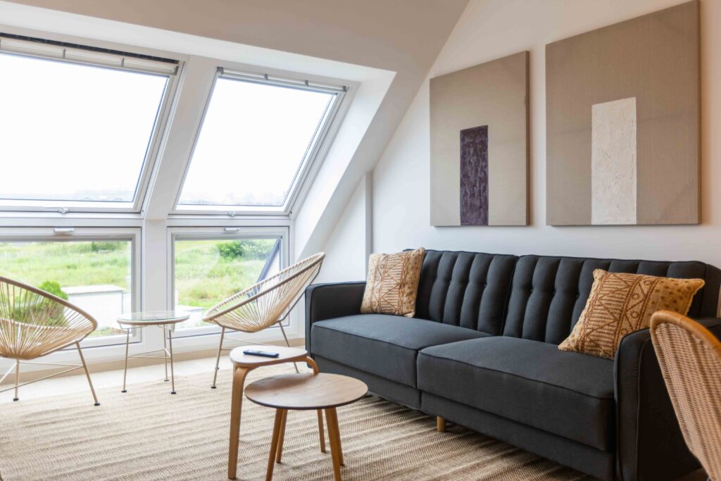 Salón abuhardillado del ático Punta dos Prados con sofá gris, sillones de ratán y ventanas Velux