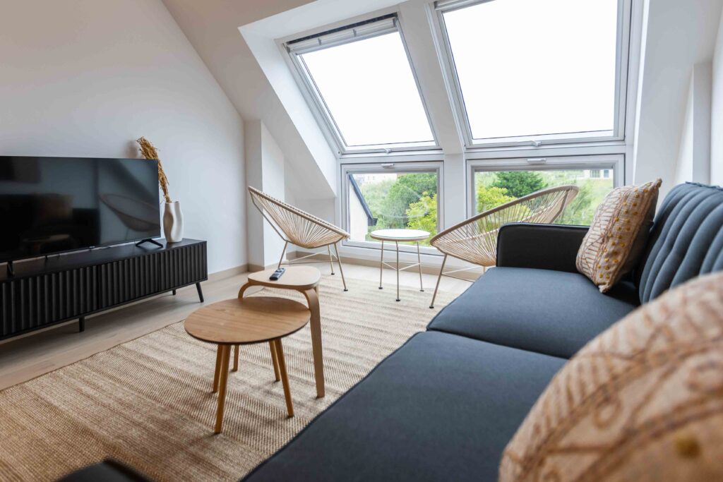 Salón de Apartagal con techo abuhardillado, ventanas Velux, sillones de ratán y sofá gris oscuro