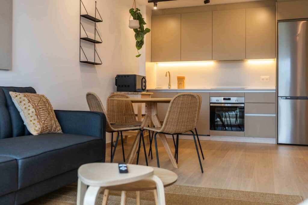Salón con sofá azul, mesa con sillas de ratán y cocina abierta en ático de Apartagal en Punta dos Prados