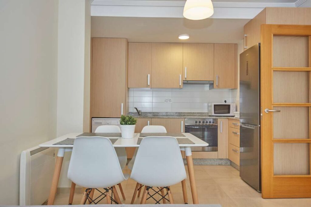 Cocina en línea con muebles en madera clara y mesa blanca con cuatro sillas en el apartamento San Miguel de Apartagal