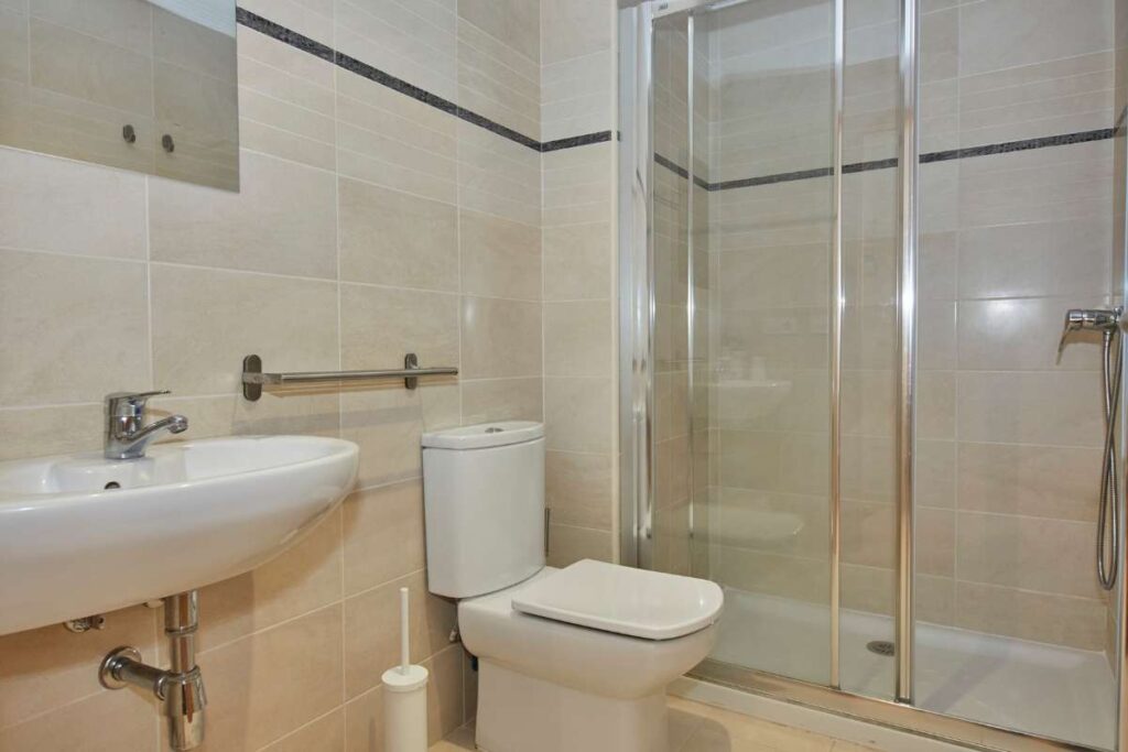 Baño con ducha de obra, mampara de cristal, inodoro y lavabo en un apartamento Apartagal en Barreiros