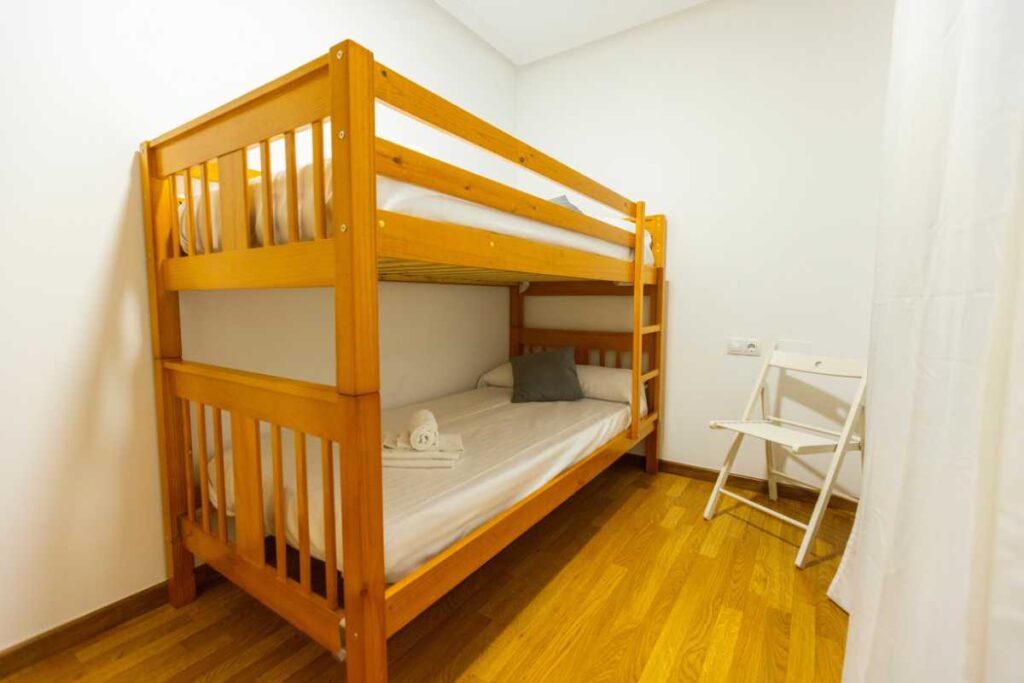 Dormitorio con litera de madera, cojines y silla plegable en apartamento de Urbanización Foz II, Apartagal