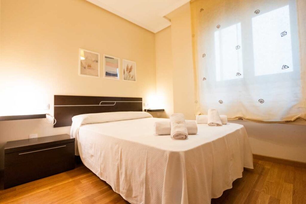 Dormitorio con cama de matrimonio, toallas enrolladas y cuadros en la pared en un apartamento de Urbanización Foz II