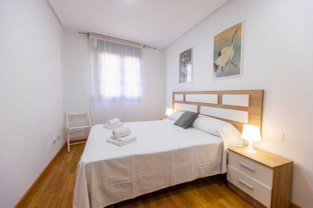 Dormitorio con cama de matrimonio, cabecero de madera, dos cuadros orientales y mesillas con lámpara
