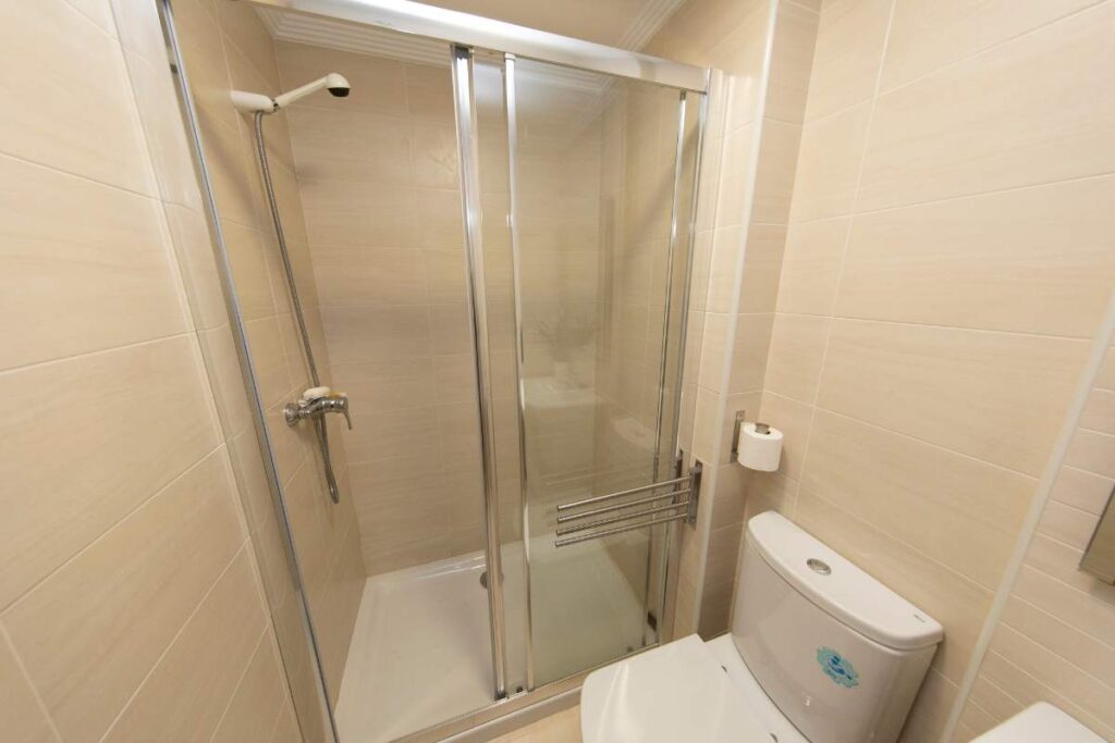 Baño con mampara de ducha corredera de cristal y azulejo beige en un apartamento de Apartagal en Foz