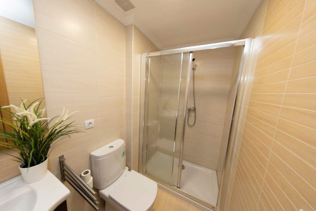 Baño con mampara de ducha, inodoro y azulejo beige en un apartamento de Apartagal en Foz