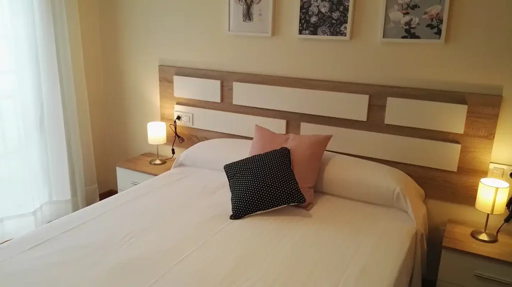 Dormitorio de matrimonio en Apartagal con cabecero de madera y blanco, cojines rosa y de topos y mesillas con lámparas