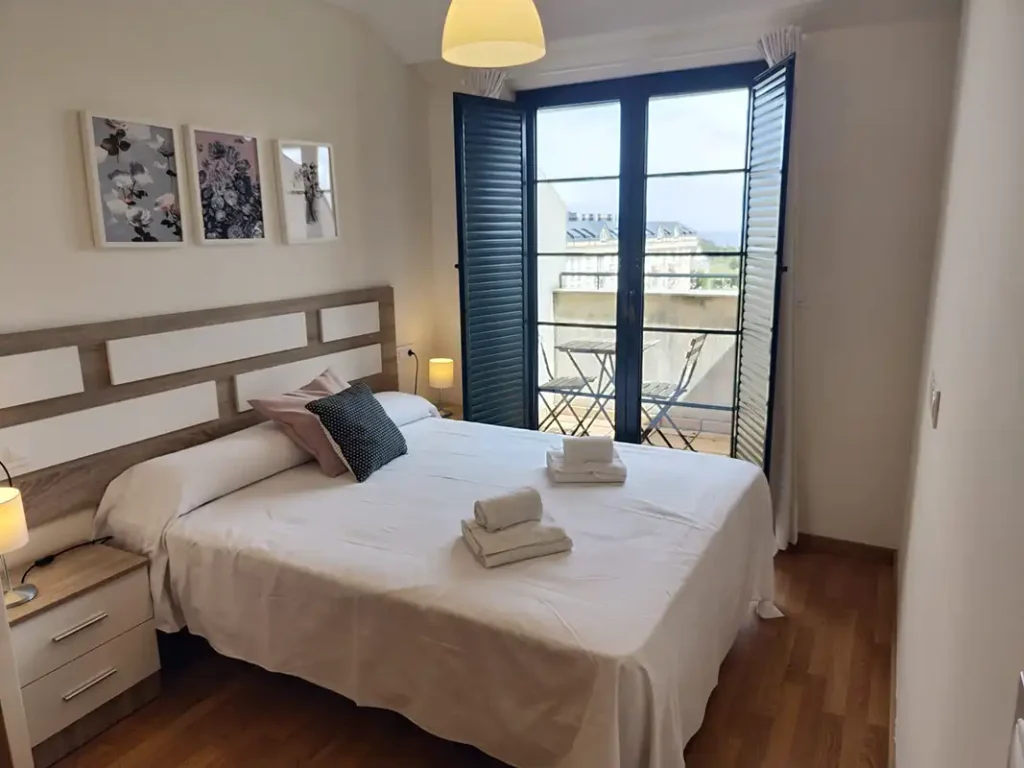 Dormitorio de matrimonio del apartamento San Miguel de Apartagal, con balcón, cuadros florales y toallas sobre la cama