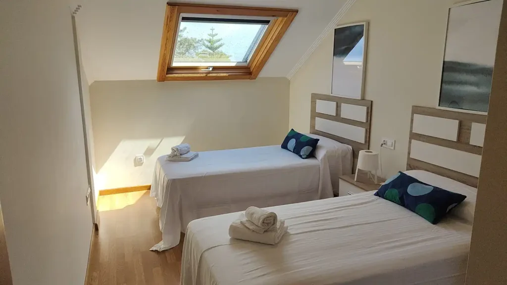 Dormitorio bajo cubierta con dos camas individuales, ventana de tejado y cabeceros de madera clara