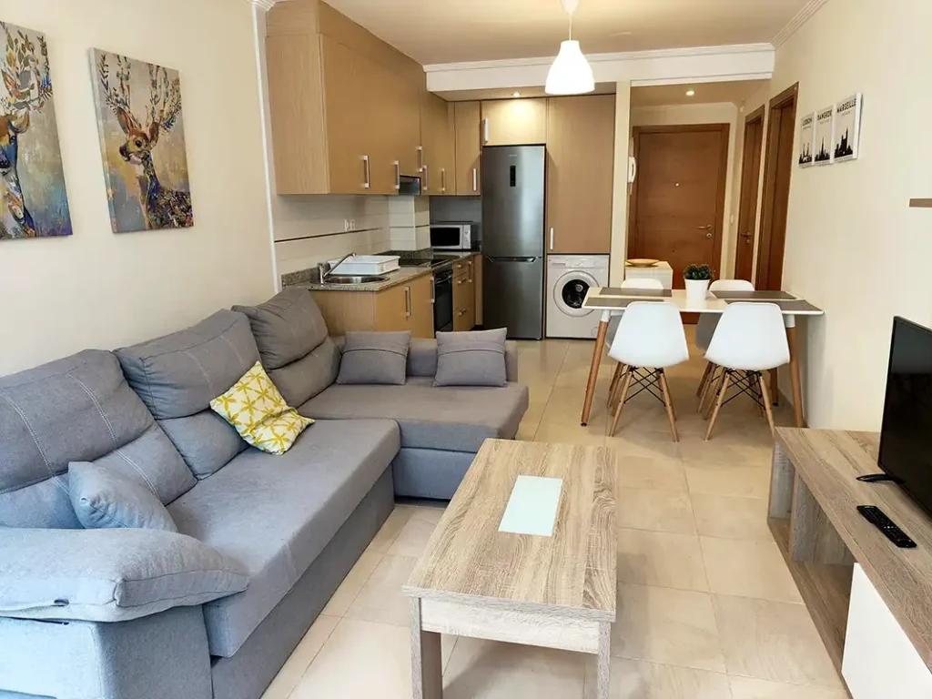 Salón comedor con cocina integrada, sofá gris y mesa blanca en el apartamento Apartagal de Barreiros