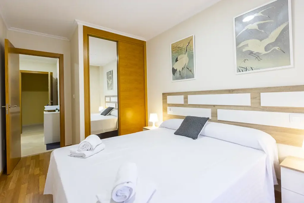 Dormitorio con cama de matrimonio, armario con espejo y toallas blancas en apartamento Apartagal Batel de Foz