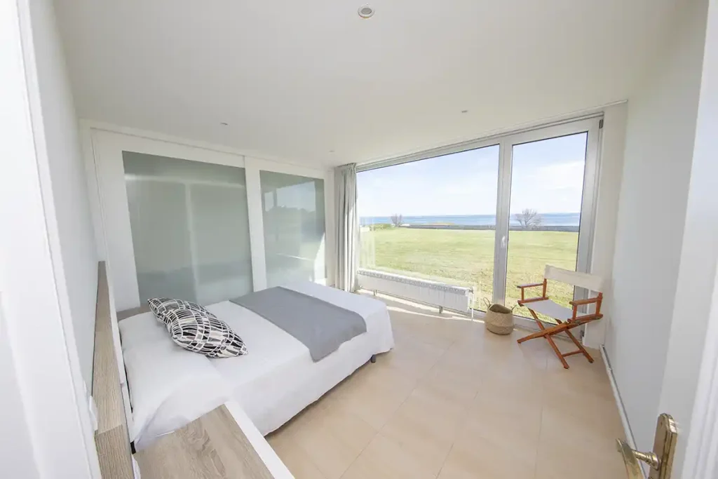 Dormitorio con cama doble, armario de puertas correderas y ventanal con vistas al mar en Foz