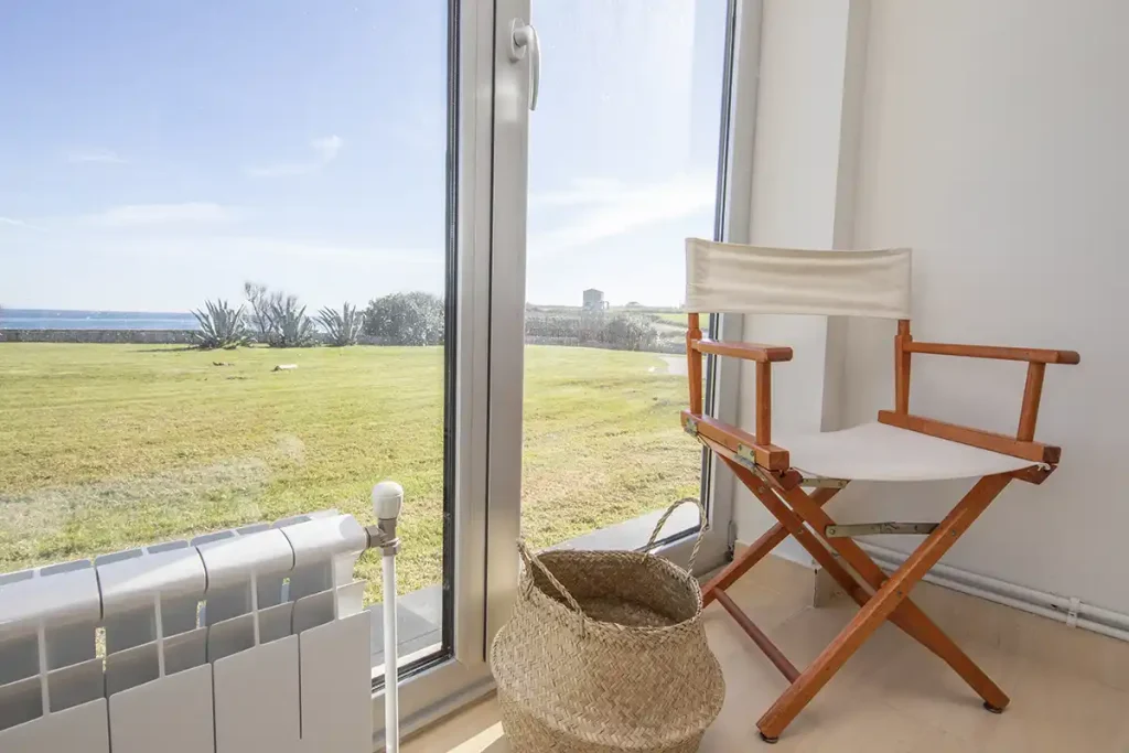 Silla de director y cesto de mimbre junto a un ventanal con vistas al mar en Foz