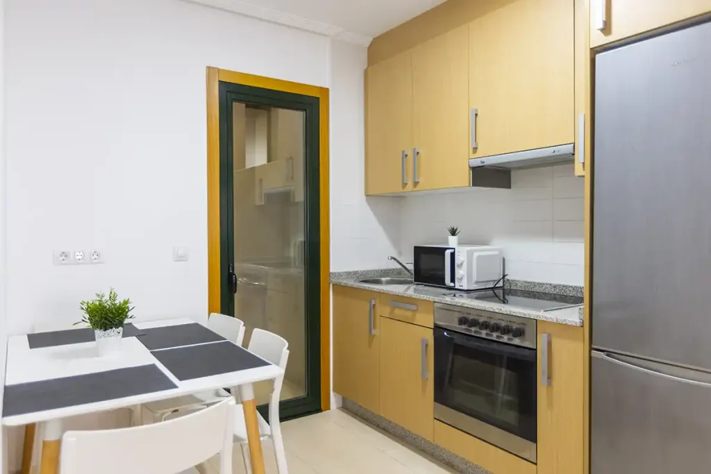 Cocina en forma de L con muebles de madera clara, frigorífico y mesa de comedor en un apartamento de Apartagal en Foz