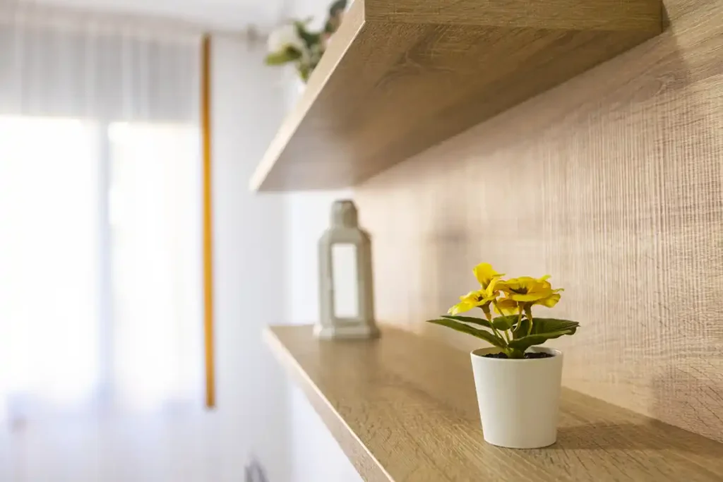 Estantería de madera con maceta de flores amarillas y farolillo decorativo junto a una ventana con cortina