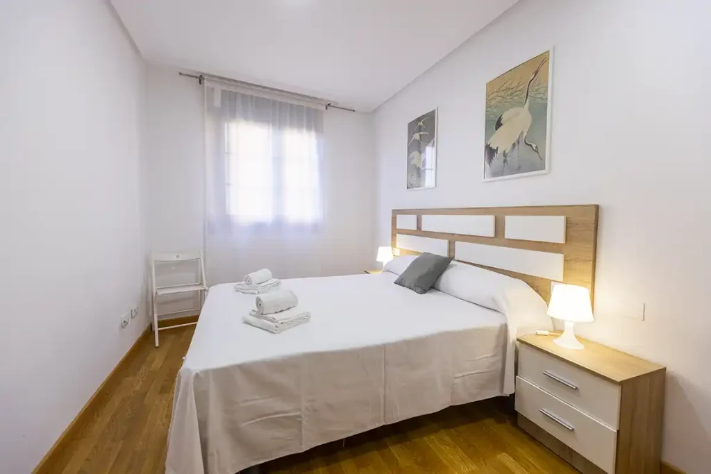 Habitación de matrimonio con cabecero de madera, dos lámparas y toallas sobre la cama en Apartagal