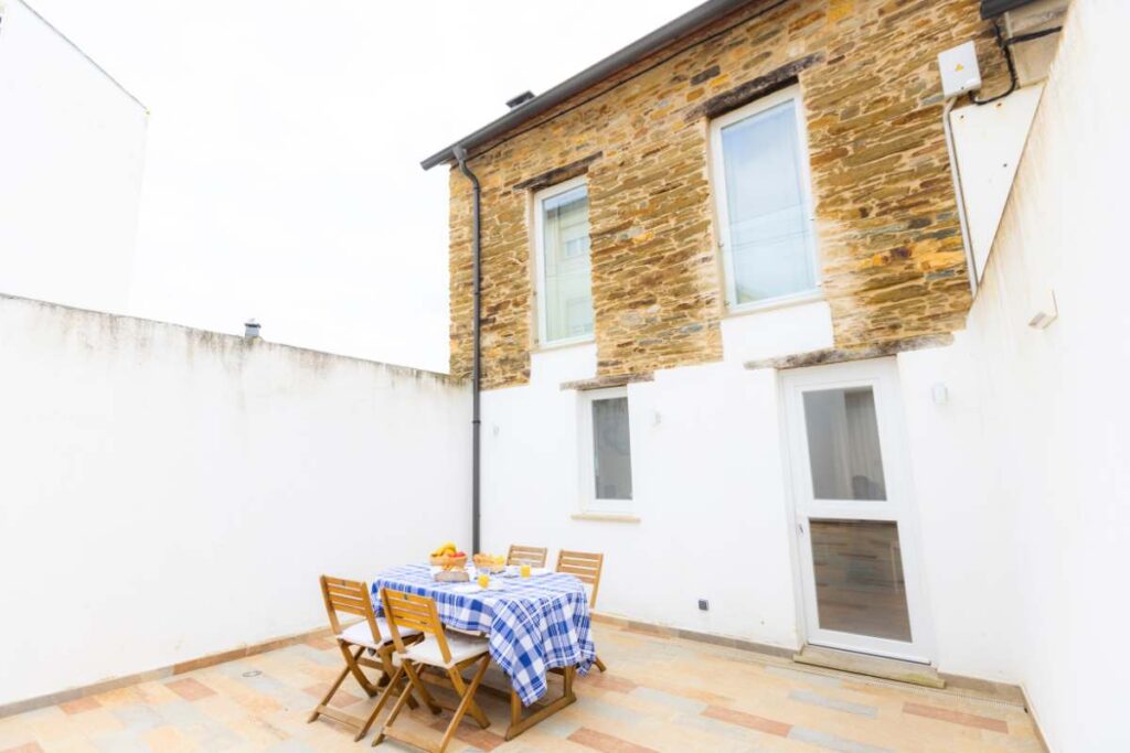 Terraza privada con suelo de piedra, mesa con mantel de cuadros azules y fachada de piedra del alojamiento Apartagal