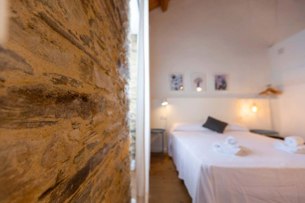 Pared de piedra en primer plano y dormitorio con cama blanca y toallas en Apartagal