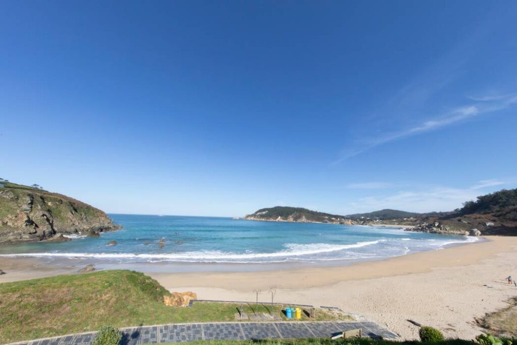 Playa de arena en una cala de Espasante con acantilados verdes y mar turquesa en calma