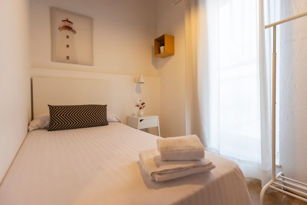 Dormitorio individual con cabecero blanco, cuadro de un faro y toallas dobladas sobre la cama