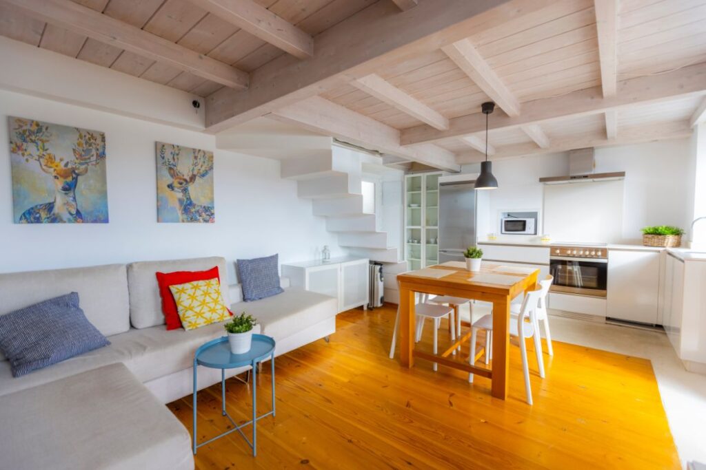 Salón con cocina abierta, techo de madera a dos aguas y mesa de comedor en un apartamento de Apartagal en Portochico