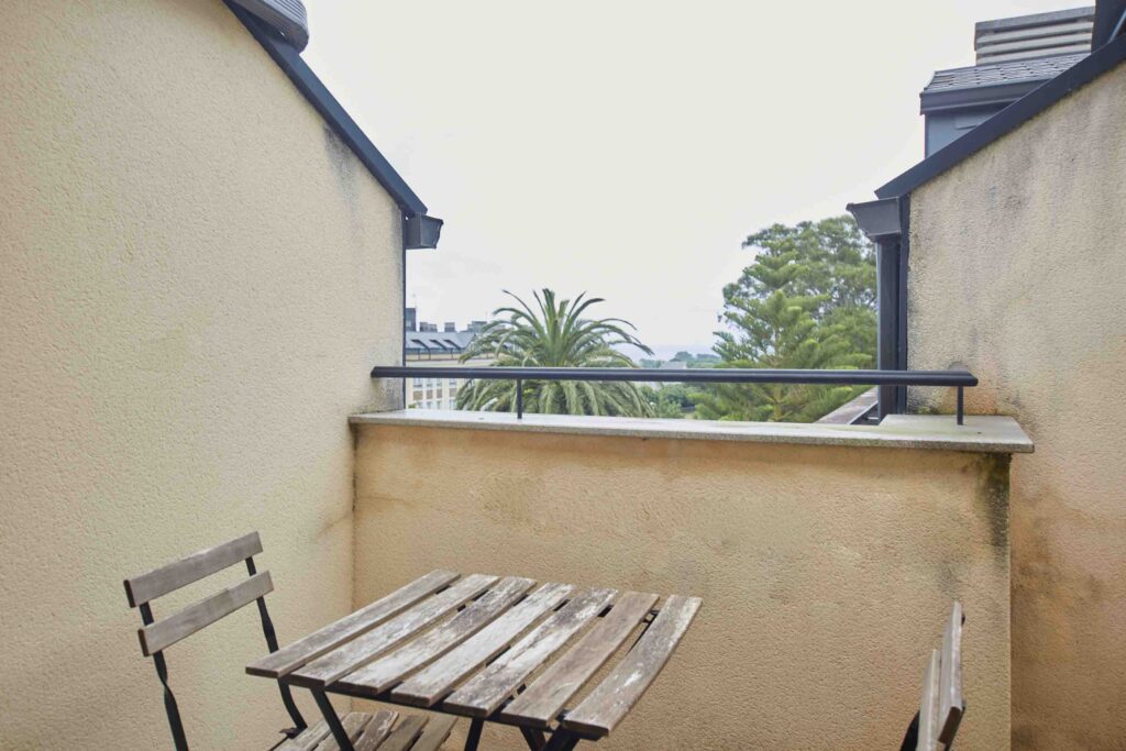 Terraza privada con mesa y sillas de madera, barandilla metálica y vistas a palmeras y arbolado del apartamento de Apartagal