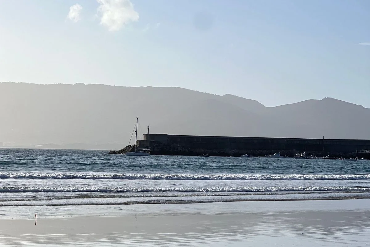 Espigón del puerto de Espasante con un velero, la ría de Ortigueira y los montes detrás