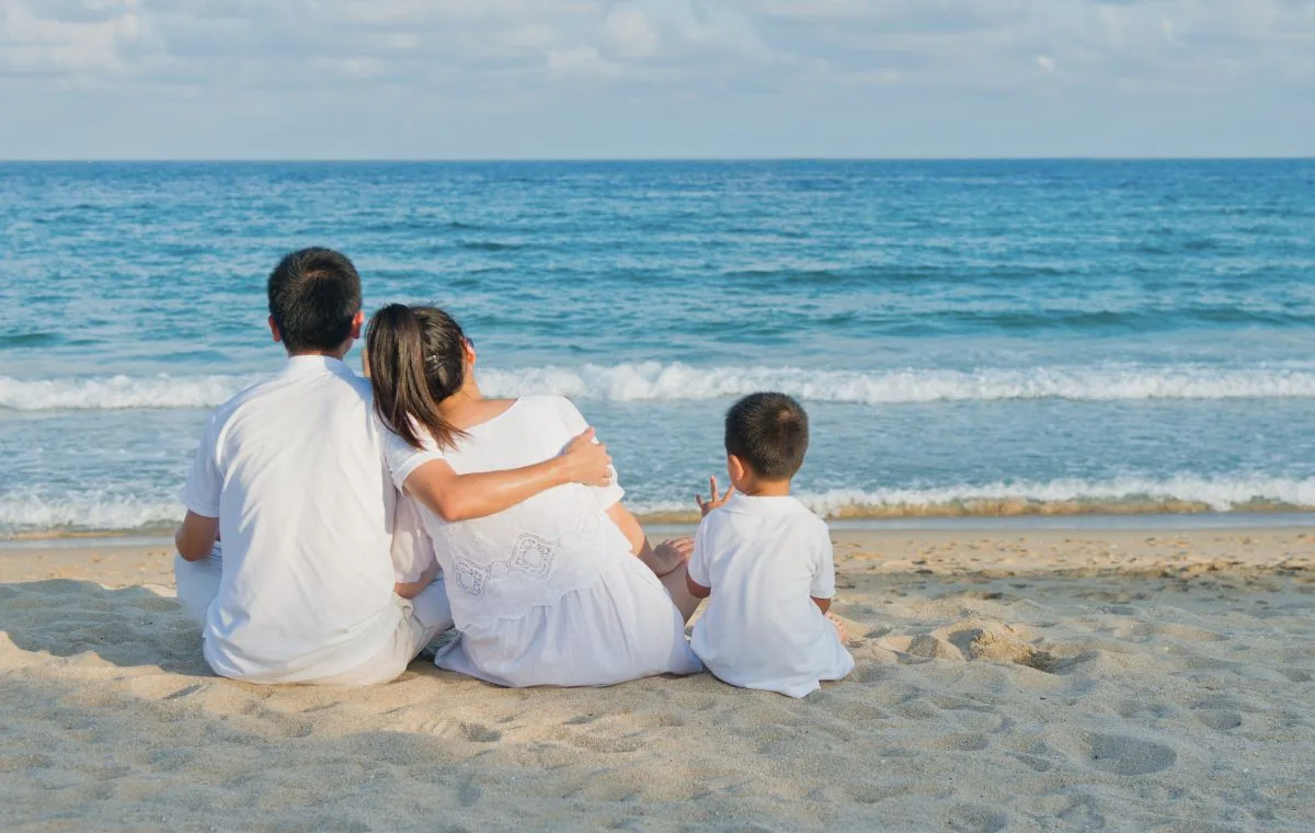 Familia sentada en la arena frente al mar en vacaciones en Galicia con niños
