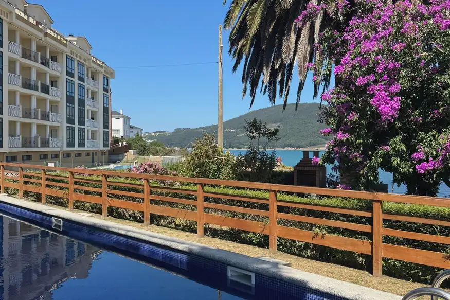 Piscina de la urbanización Mar de Vicedo con palmera, buganvilla y vistas a la ría de O Vicedo