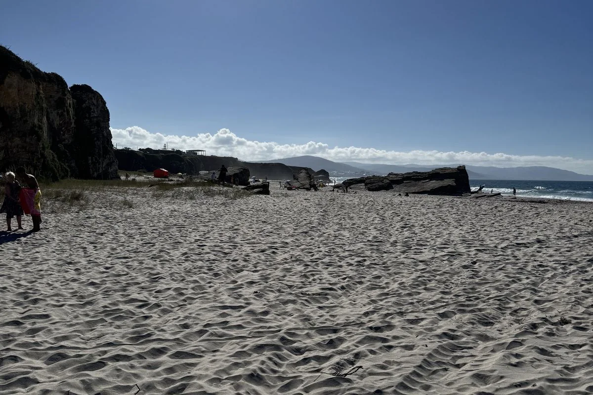 Playa de arena fina con acantilados y rocas al fondo en la costa de Barreiros