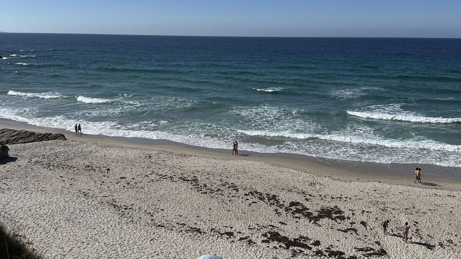 Playa de Barreiros vista desde arriba, con olas, arena y gente paseando por la orilla