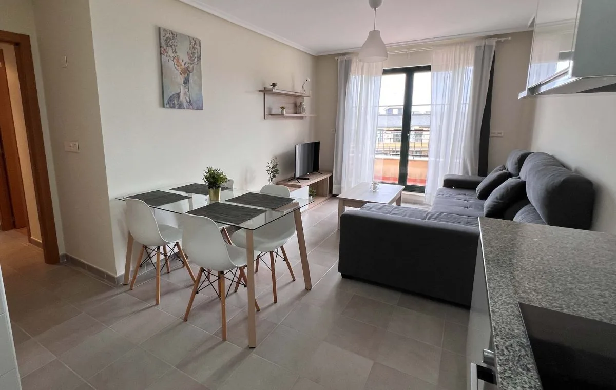 Salón comedor con sofá, mesa para cuatro y cocina de un apartamento familiar de Apartagal