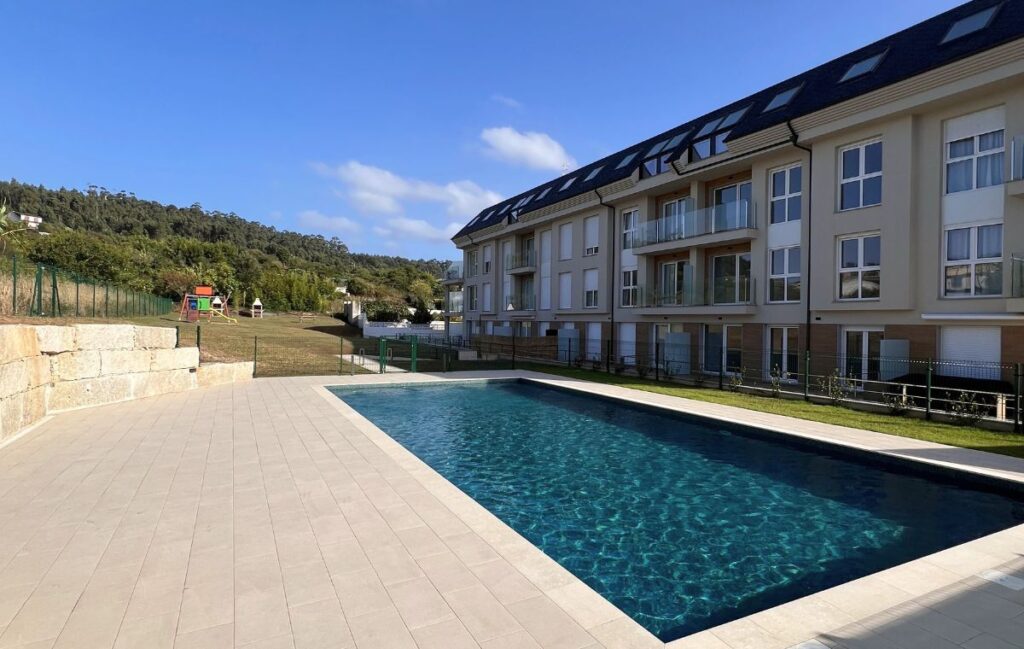 Piscina exterior con césped y zona de juegos infantiles junto al edificio de apartamentos Punta dos Prados de Apartagal