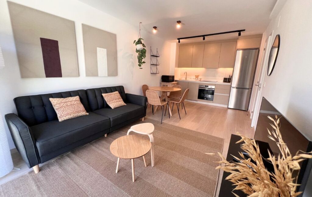Salón con sofá negro, mesa de comedor y cocina abierta en un apartamento de Apartagal en Punta dos Prados