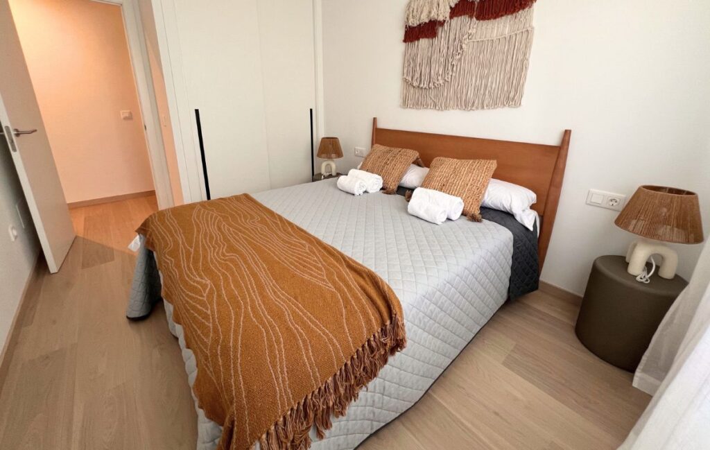 Dormitorio de matrimonio en Apartagal con cabecero de madera, manta mostaza y tapiz de macramé en la pared